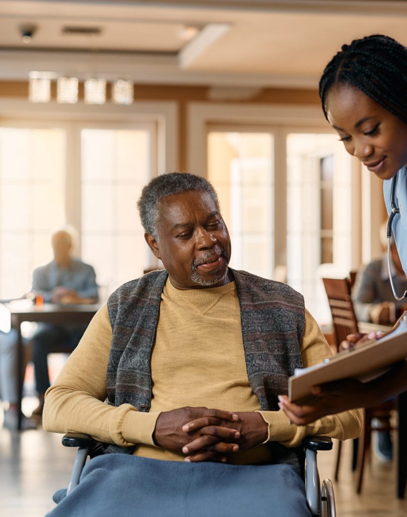 Senior black man in wheelchair and young nurse analyzing medical paperwork at nursing home.